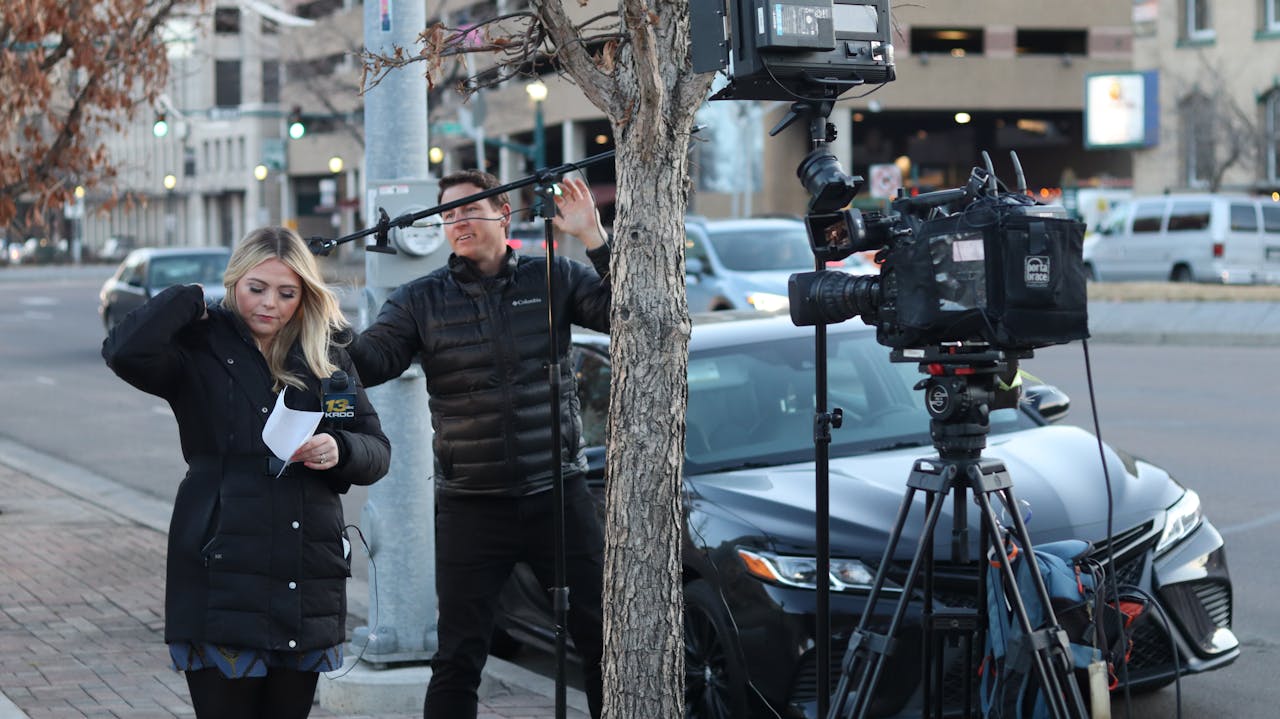 News crew setting up equipment on city street, capturing urban life.