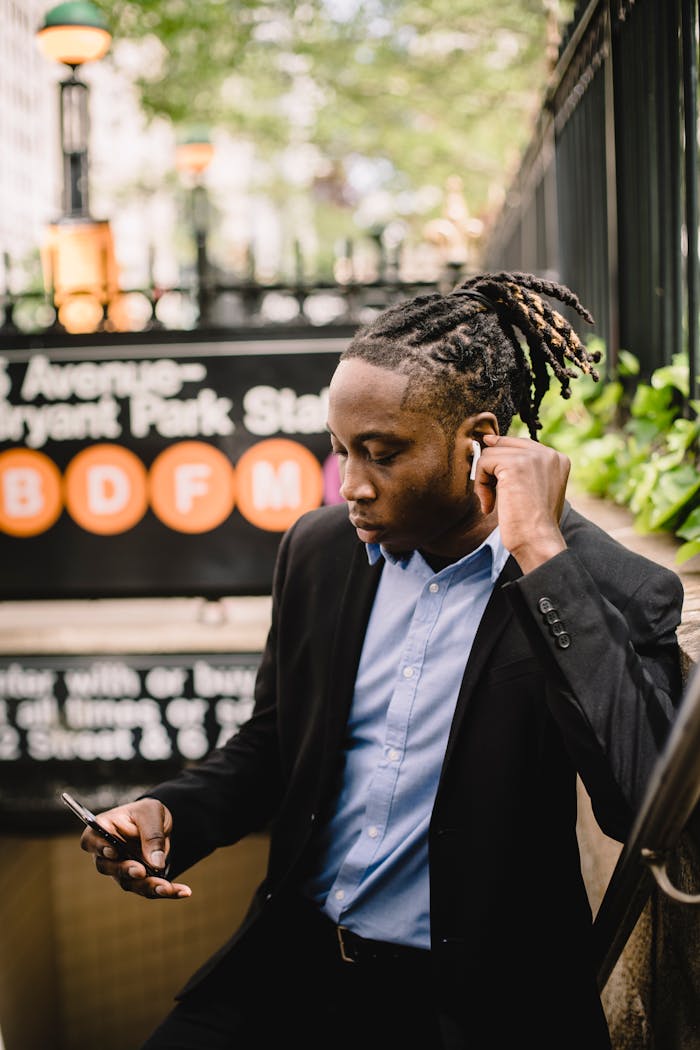 services-02 Young professional man with earbuds using phone outside a subway entrance in a city setting.